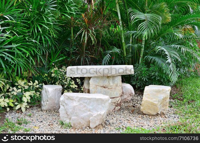Marble chair on pebbles in garden with tree background.