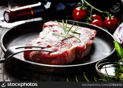 Marbled beef steak in a frying pan with a bottle of wine and vegetables on old wood background