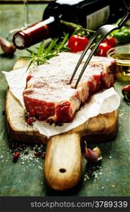 Marbled beef steak with a bottle of wine and vegetables on old wood background
