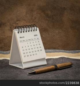 March 2022 - spiral desktop calendar against abstract paper landscape, time and business concept