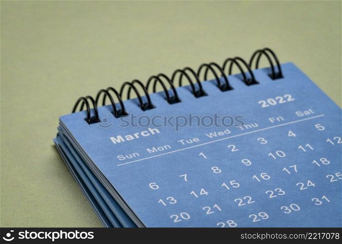 March 2022 - spiral desktop calendar against textured paper, time and business concept