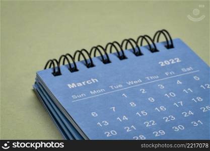 March 2022 - spiral desktop calendar against textured paper, time and business concept