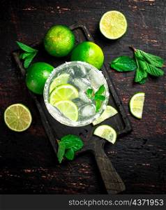 Margarita on a cutting board with pieces of lime and mint leaves. On a rustic dark background. High quality photo. Margarita on a cutting board with pieces of lime and mint leaves.