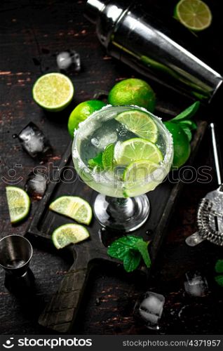 Margarita on a cutting board with pieces of lime and mint leaves. On a rustic dark background. High quality photo. Margarita on a cutting board with pieces of lime and mint leaves.