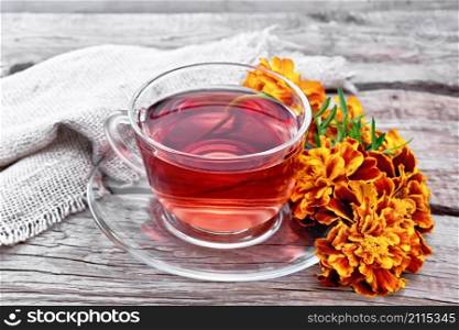 Marigold herbal tea in a glass cup and saucer, fresh flowers, sackcloth napkin on wooden board background
