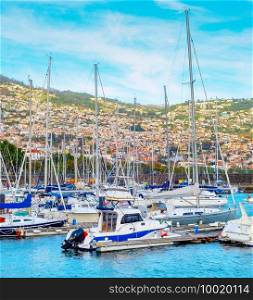 Marina with moored yachts and motorboats in evening sunlight, Funchal cityscape on mountains in background, Madeira island, Portugal