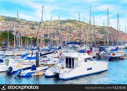 Marina with white yachts and motorboats, Funchal cityscape on hill in background, Madeira, Portugal