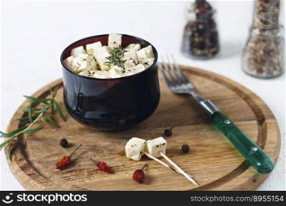 Marinated feta in a plate on a wooden board with spices on a white background.. Marinated feta in a plate on a wooden board with spices on a white background