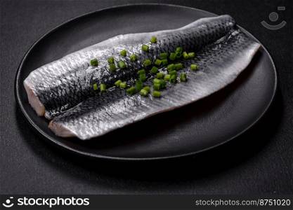 Marinated fillet with spices and herbs of sea herring on a black plate against a dark concrete background. Marinated fillet with spices and herbs of sea herring on a black plate