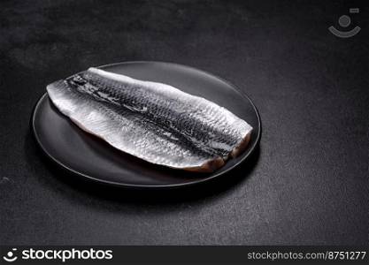 Marinated fillet with spices and herbs of sea herring on a black plate against a dark concrete background. Marinated fillet with spices and herbs of sea herring on a black plate