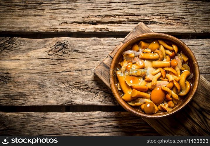 Marinated mushrooms in a bowl on the Board. On wooden background.. Marinated mushrooms in a bowl on the Board.