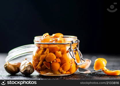 Marinated mushrooms in a glass jar with cloves of garlic. On a black background. High quality photo. Marinated mushrooms in a glass jar with cloves of garlic.