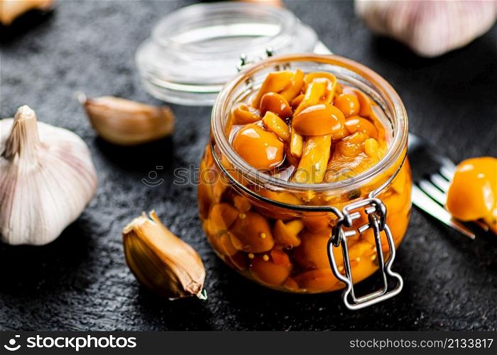Marinated mushrooms in a glass jar with cloves of garlic. On a black background. High quality photo. Marinated mushrooms in a glass jar with cloves of garlic.