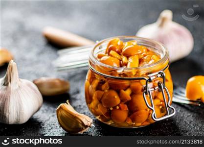 Marinated mushrooms in a glass jar with cloves of garlic. On a black background. High quality photo. Marinated mushrooms in a glass jar with cloves of garlic.