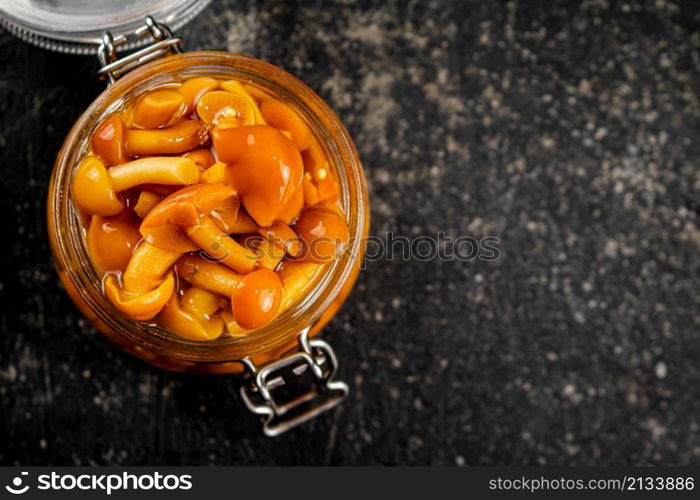 Marinated mushrooms in an open glass jar. On a black background. High quality photo. Marinated mushrooms in an open glass jar.