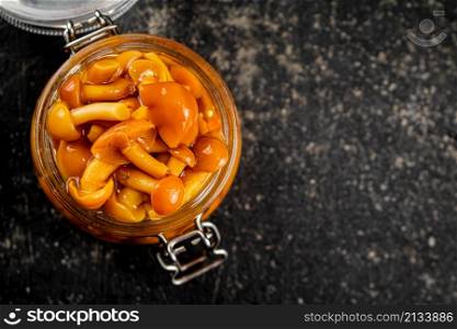 Marinated mushrooms in an open glass jar. On a black background. High quality photo. Marinated mushrooms in an open glass jar.