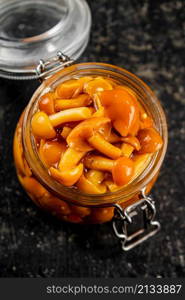 Marinated mushrooms in an open glass jar. On a black background. High quality photo. Marinated mushrooms in an open glass jar.