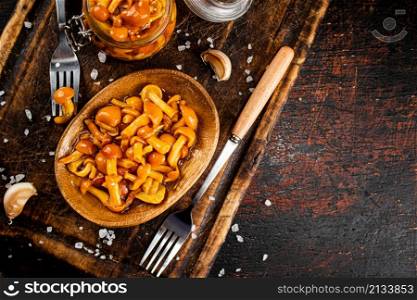 Marinated mushrooms on a wooden plate. On a rustic dark background. High quality photo. Marinated mushrooms on a wooden plate.