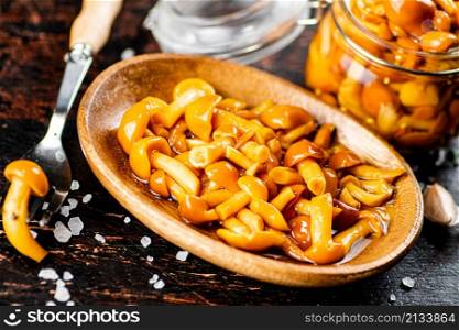 Marinated mushrooms on a wooden plate. On a rustic dark background. High quality photo. Marinated mushrooms on a wooden plate.