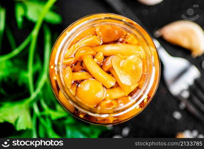 Marinated mushrooms with a glass jar with parsley and garlic. On a black background. High quality photo. Marinated mushrooms with a glass jar with parsley and garlic.