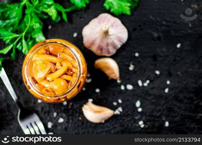 Marinated mushrooms with a glass jar with parsley and garlic. On a black background. High quality photo. Marinated mushrooms with a glass jar with parsley and garlic.