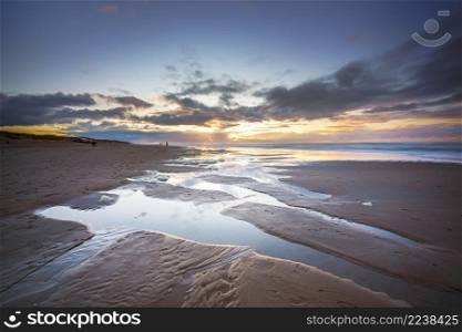 Maritime landscape at sunset with reflection of clouds in low tide water, Waddenzee, Texel, The Netherlands. Sunset over beach at North sea coast