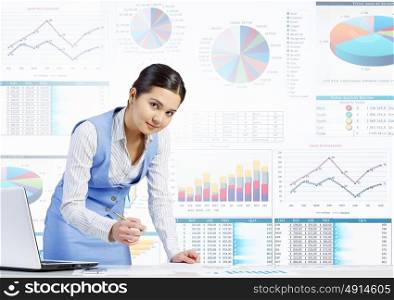 Market analysis and report. Businesswoman standing at table and writing with pen and infographs at background