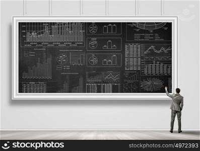 Marketing sales strategy. Rear view of businessman drawing infographs on chalkboard