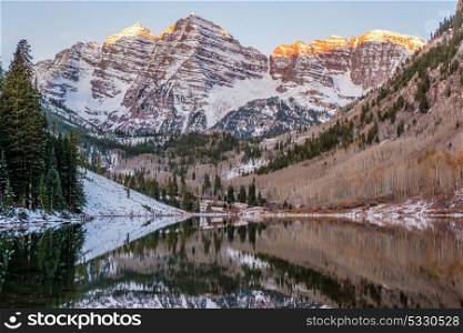 Maroon Bells and Maroon Lake with reflection of rocks and mountains in snow at sunrise around at autumn in Colorado, USA.