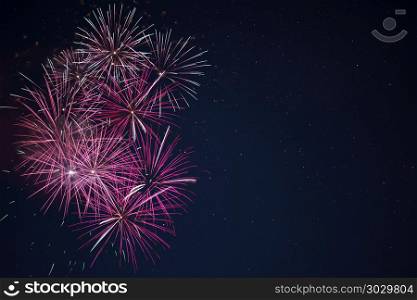 Maroon red pink celebration fireworks over night sky. Beautiful maroon red pink celebration fireworks located left side over night sky, copy space. Independence Day, 4th of July, New Year holidays salute background.