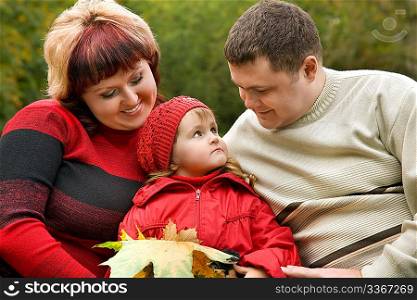 Married couple and little girl sit on a bench in park in autumn