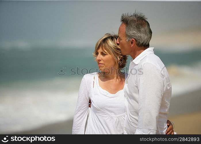 Married couple dressed in white taking a walk along the beach