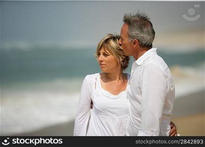 Married couple dressed in white taking a walk along the beach