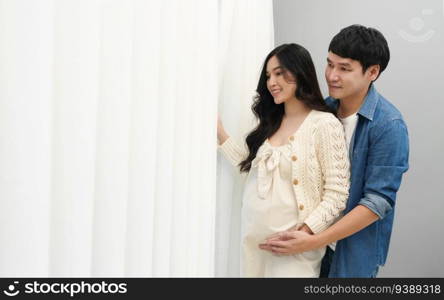 married couple is expecting baby. man embracing and talking with his pregnant wife while looking view through the window at home