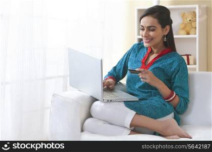 Married Indian woman home shopping with laptop and credit card in living room