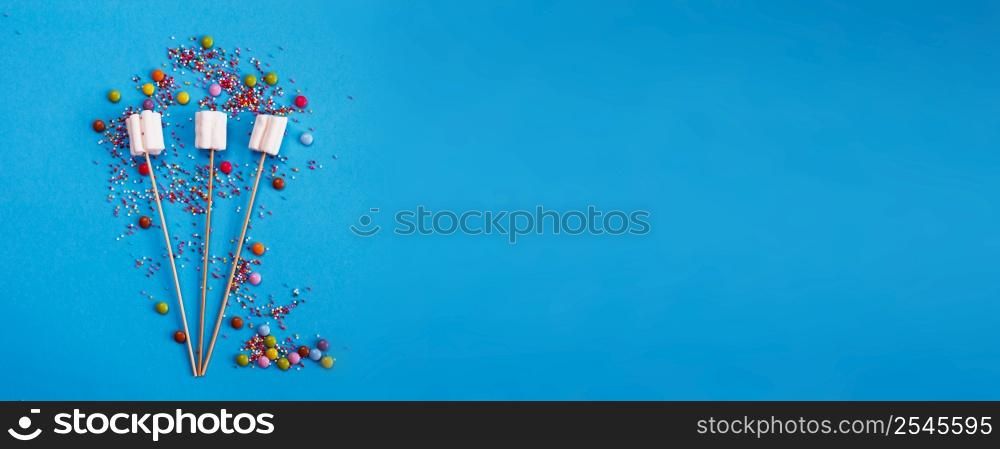 marshmallows composition on wooden skewers on a blue background. Flat lay, holiday concept. bouquet of sweets. banner. marshmallows composition on wooden skewers on blue background. Flat lay, holiday concept. bouquet of sweets. banner