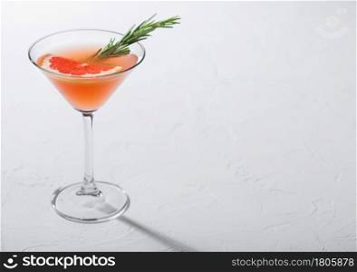 Martini glass with summer red grapefruit cocktail with fruit slice and rosemary on white background. Space for text