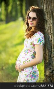 Marvelous pregnant mom leaning against the tree