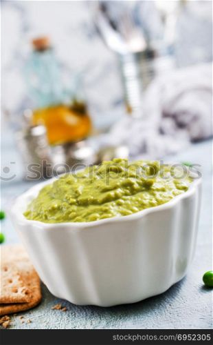 Mashed green peas and olive oil in a ceramic bowl on a table. Healthy vegetarian food