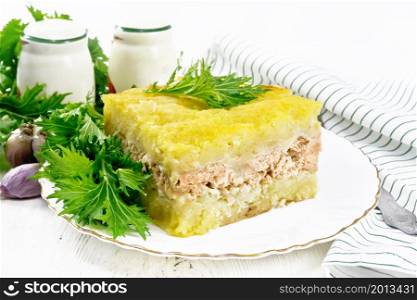 Mashed potato casserole with salmon fillet and lettuce in a plate, kitchen towel, garlic on the background of a light wooden board
