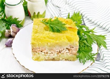 Mashed potato casserole with salmon fillet and lettuce in a plate, towel, garlic on a white wooden board background