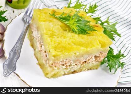 Mashed potato casserole with salmon fillet and lettuce in a plate, towel, garlic on the background of a light wooden board