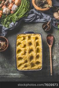 Mashed potato in casserole with spoon on dark rustic kitchen table background with ingredients and vintage utensils. Top view. Tasty home cuisine