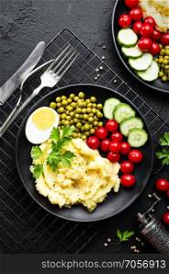 Mashed potato with green peas, tomatoes and boiled egg. Potato puree on plate with vegetables and egg