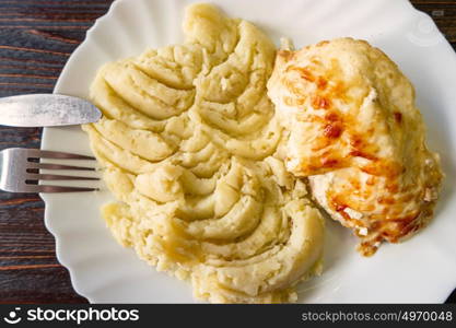 Mashed potatoes and chicken on plate with fork and knife top view