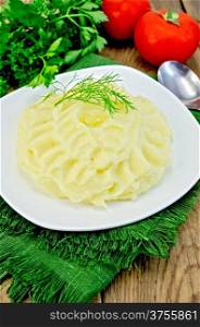 Mashed potatoes with butter in a plate on a napkin, tomatoes, parsley, dill on a wooden boards background