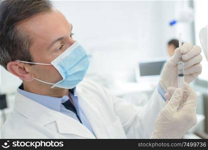 masked male doctor removing protective sheath from syringe