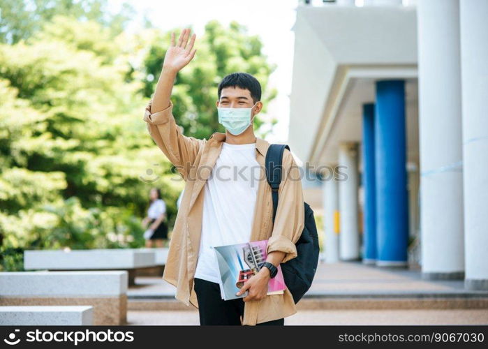 Masked men carry books and backpack on stairs and raise their right hands up.