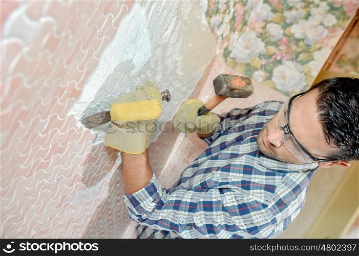 Mason chiping away at surface of a wall