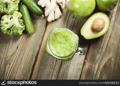 Mason jar mug filled with green smoothie and ingredients on wooden rustic table. Green healthy food, vegetarian, clean eating concept. Top view, copyspace